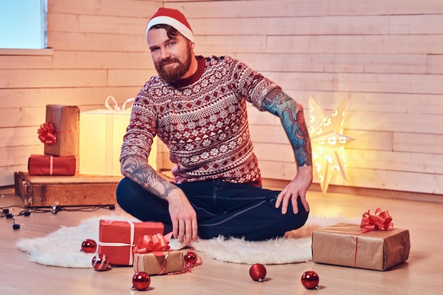 Redhead bearded male in Santa hat in a room with Christmas decoration.