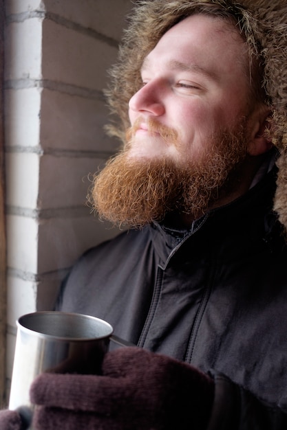 ホットコーヒーや紅茶のカップを保持している極ジャケットの赤毛のひげを生やした男