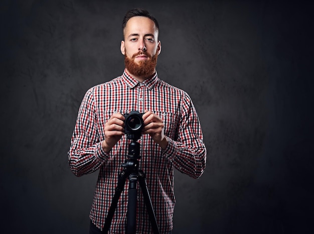 Redhead bebaarde fotograaf houdt digitale camera en een statief.