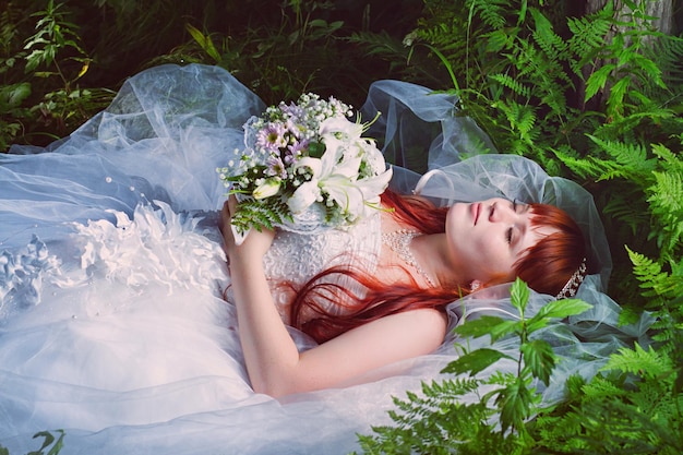 Redhead bride lying on the green grass