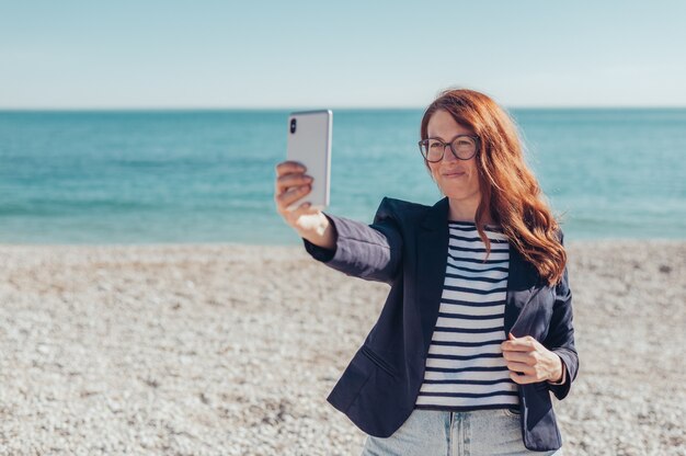 Donna d'affari rossa che usa il telefono in riva al mare