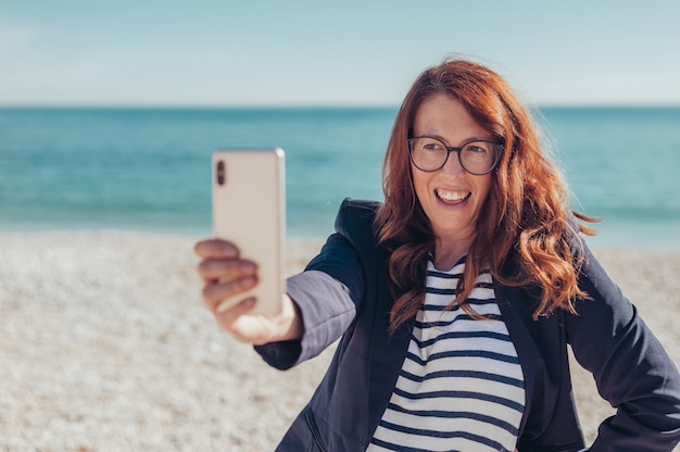 Donna d'affari rossa che usa il telefono in riva al mare