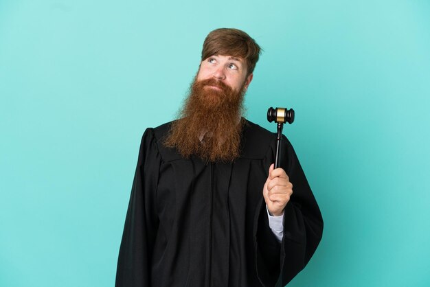 Redhead caucasian judge man isolated on blue background and looking up