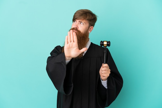 Redhead caucasian judge man isolated on blue background making stop gesture and disappointed