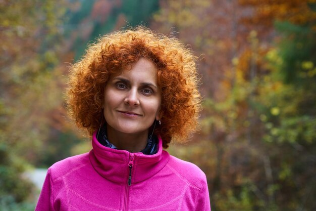 Redhead caucasian woman walking in the forest on an alley
covered in fallen leaves