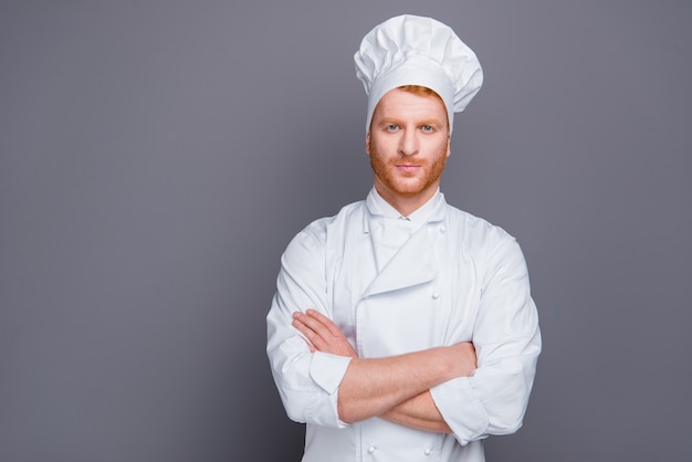 Redhead chef in uniform posing against the grey wall