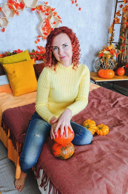 redhead curly young woman in warm sweater sits in bed at a cozy home, laughing. autumn decorations