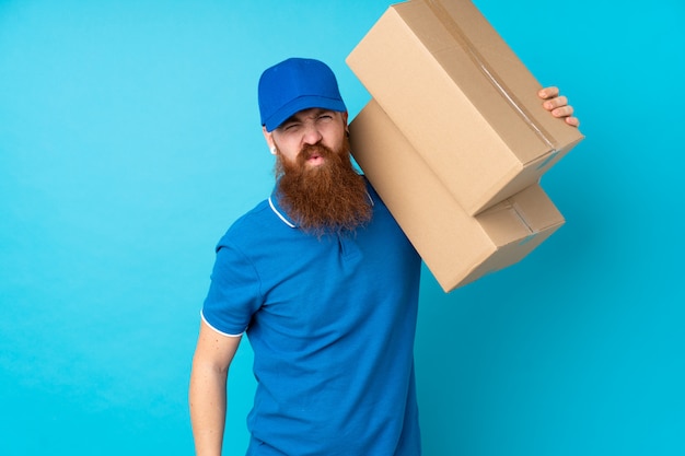 Redhead delivery man over isolated blue wall