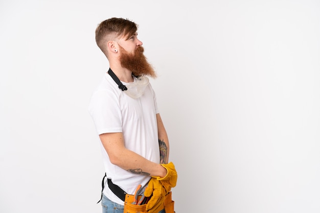 Redhead electrician man with long beard over isolated white wall looking side