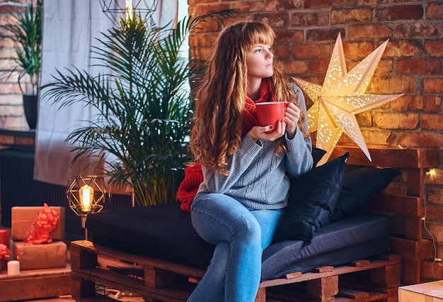 Redhead female drinks a hot coffee in a living room with loft interior.