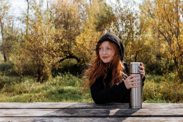 Redhead girl at an autumn picnic is going to drink tea