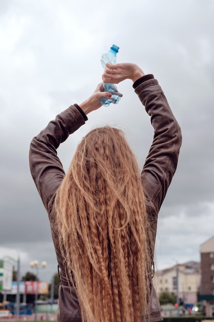 Redhead girl compressing in hand used plastic bottle before throw out that garbage to trash. Garbage recycle concept