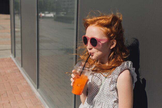 플라스틱 유리에서 레모네이드를 마시는 빨강 머리 소녀.