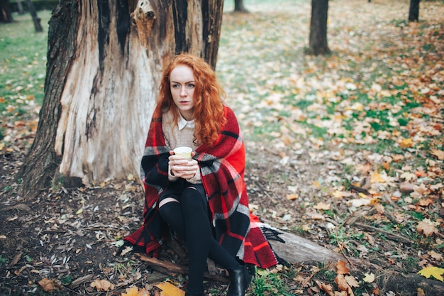 秋の公園でコーヒーを持っている赤毛の女の子