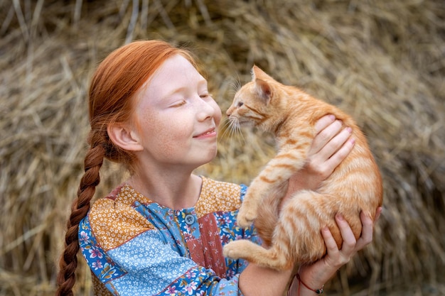 彼女の腕に生姜の子猫を保持している赤毛の女の子