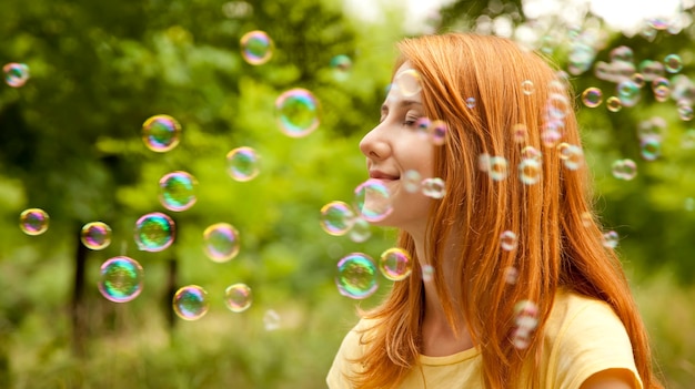 Фото Рыжая девушка в парке под дождем мыльных пузырей.