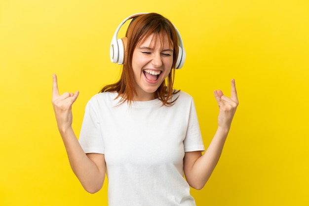 Ragazza rossa isolata su sfondo giallo che ascolta musica facendo un gesto rock