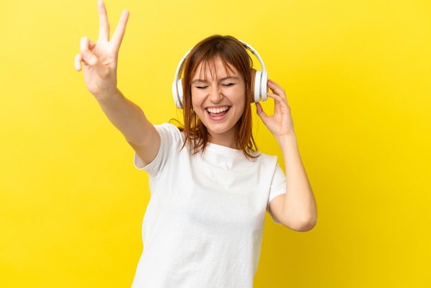 Redhead girl isolated on yellow background listening music and singing