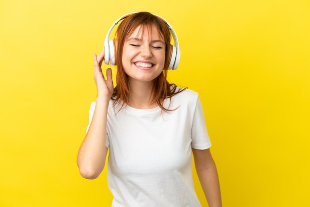 Redhead girl isolated on yellow background listening music