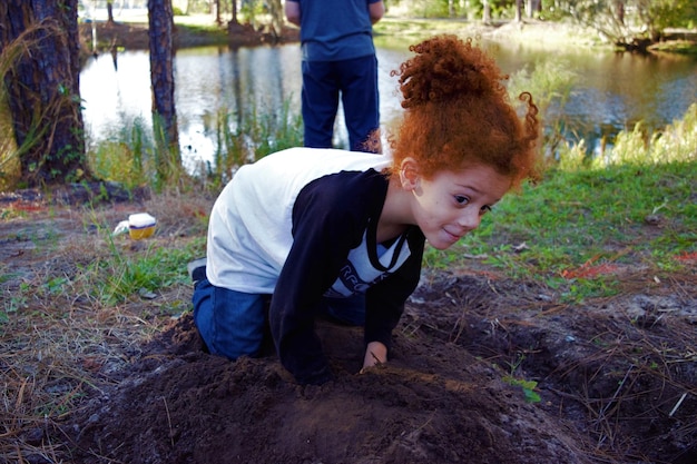 Фото Рыжая девушка играет в грязи против пруда