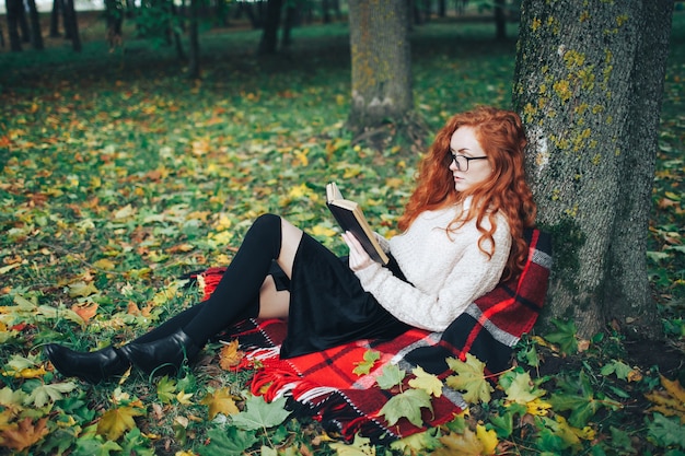 redhead girl reading the book in autumn park 