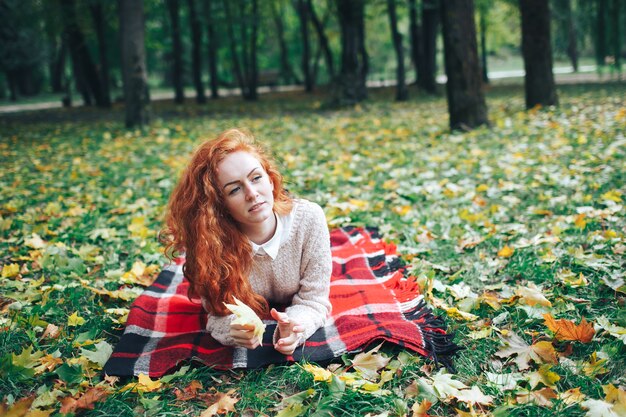 рыжая девушка на красном плед в осеннем парке