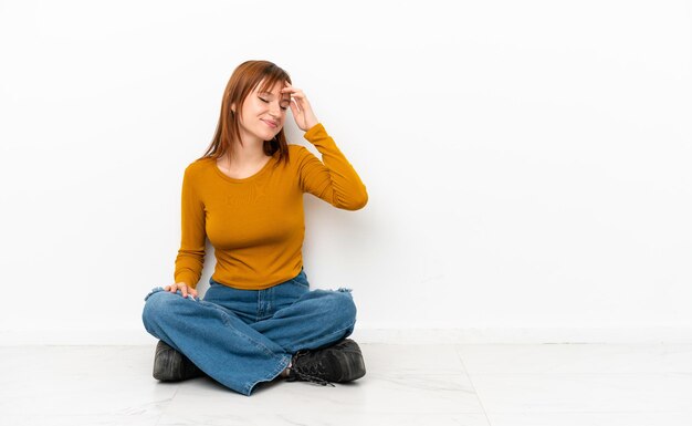 Redhead girl sitting on the floor isolated on white background laughing