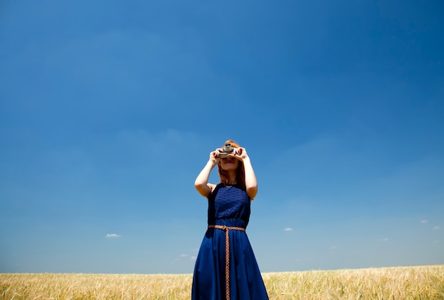 Foto ragazza rossa al campo primaverile con fotocamera retrò.