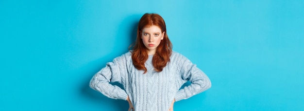 Redhead girl staring angry and displeased at camera frowning upset standing against blue background