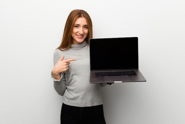 Redhead girl over white wall showing a laptop