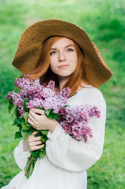 Redhead girl with a bouquet of lilacs in a spring garden