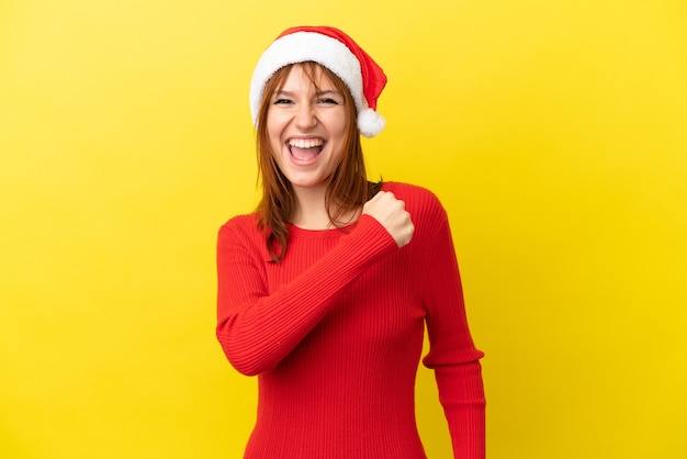 勝利を祝う黄色の背景に分離されたクリスマス帽子と赤毛の少女