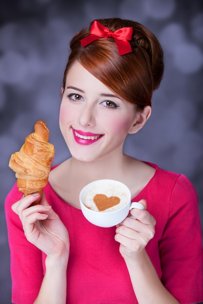 Redhead girl with croissant and cup of coffee