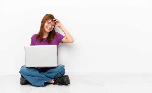 Redhead girl with a laptop sitting on the floor laughing