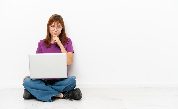 Ragazza rossa con un computer portatile seduto sul pavimento pensando