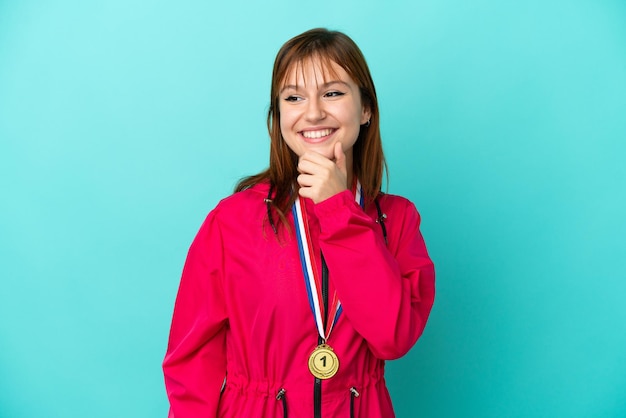 Redhead girl with medals isolated o blue background looking to the side