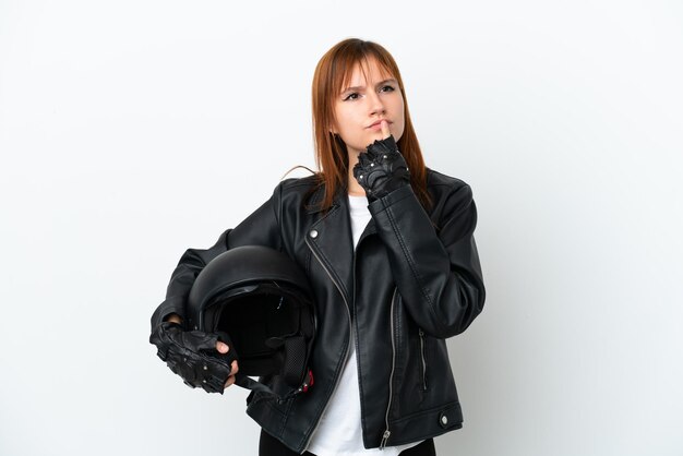 Redhead girl with a motorcycle helmet isolated on white background having doubts while looking up