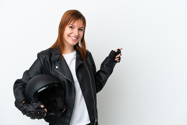Redhead girl with a motorcycle helmet isolated on white\
background pointing finger to the side