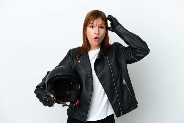 Рыжая девушка в мотоциклетном шлеме на белом фоне с удивленным выражением лица