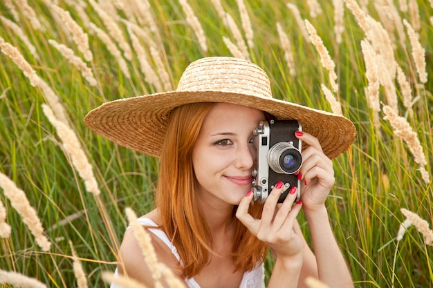 Redhead girl with old camera in meadow.