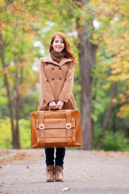 秋の屋外でスーツケースと赤毛の女の子