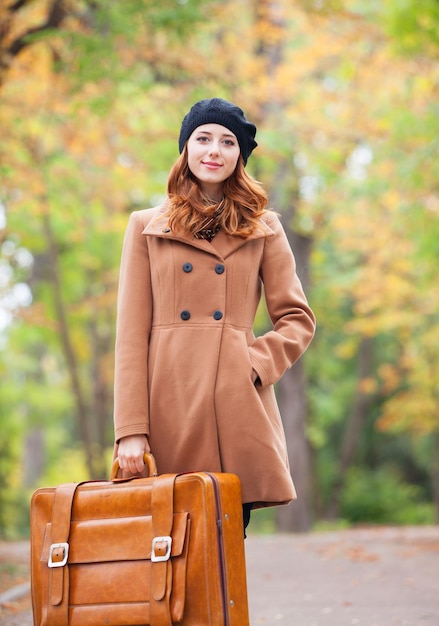 Redhead girl with suitcase at autumn outdoor