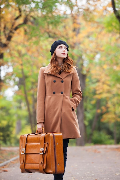 Redhead girl with suitcase at autumn outdoor