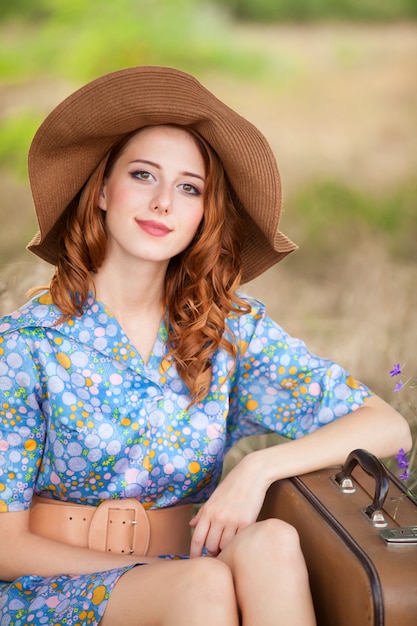 Redhead girl with suitcase sitting at autumn grass