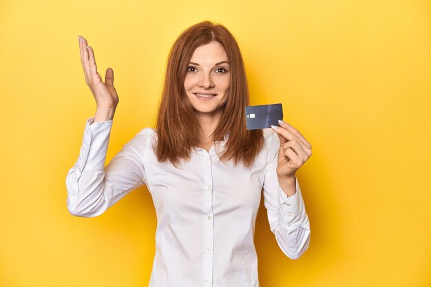 Photo redhead holding credit card financial concept receiving a pleasant surprise excited
