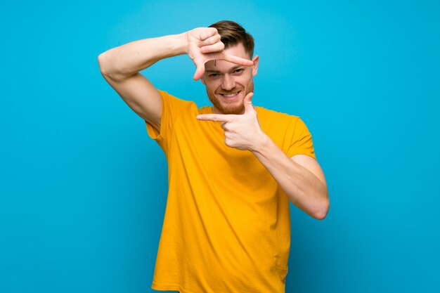 Redhead man over blue wall focusing face. Framing symbol