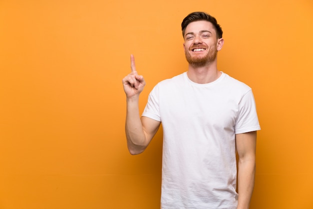 Redhead man over brown wall showing and lifting a finger in sign of the best