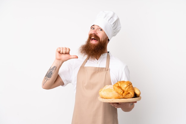 Redhead man in chef uniform. Male baker holding a table with several breads proud and self-satisfied