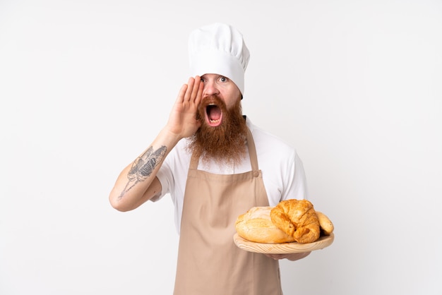 Redhead man in chef uniform. Male baker holding a table with several breads shouting with mouth wide open