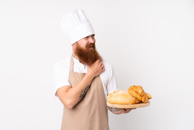 Redhead man in chef uniform. Male baker holding a table with several breads thinking an idea and looking side